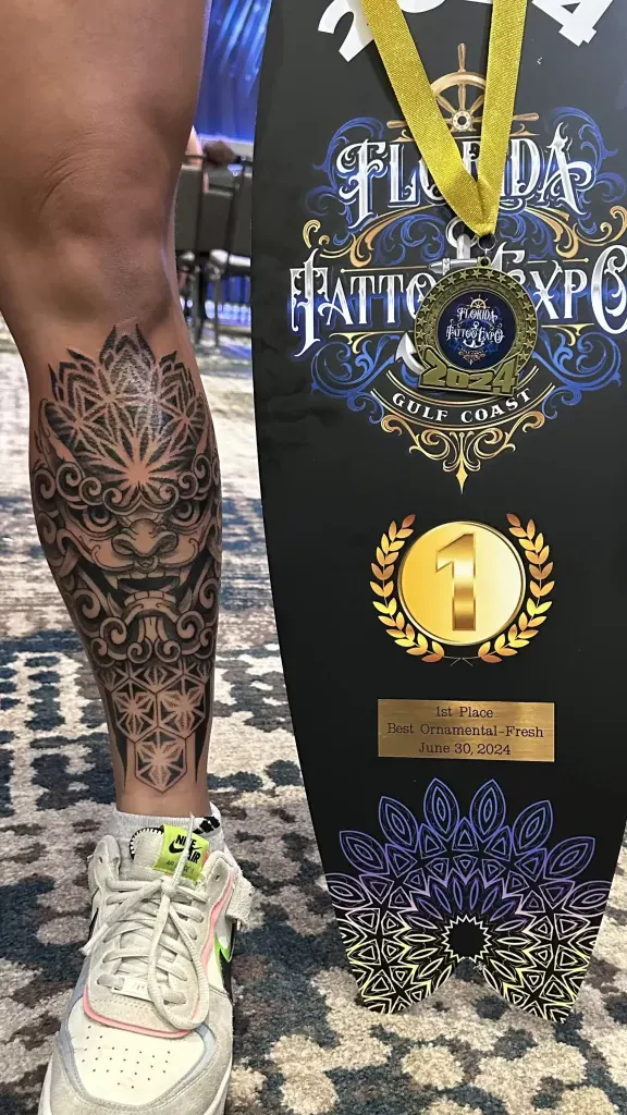 Award-winning ornamental leg tattoo next to the 1st place trophy of the Florida Tattoo Expo 2024, by Duk Tattoo